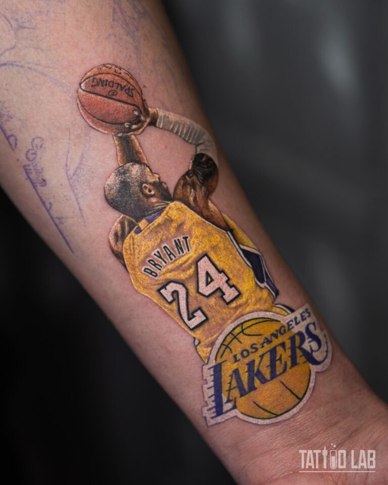Colour realism tattoo detail of Kobe Bryant taking a jump shot in a gold jersey above the Lakers logo on the forearm