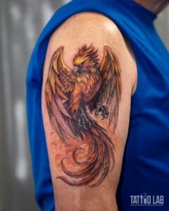 Colour realism phoenix tattoo with spread wings and curling red tail feathers on the upper arm