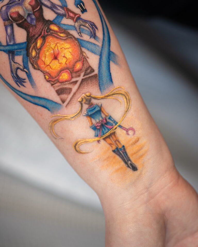 Close-up of a colour Sailor Moon tattoo with long golden twin tails and a moon wand below a glowing orange crystal core