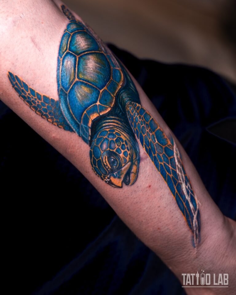 Sea turtle tattoo in blue and yellow-orange colour with a glossy shaded shell on forearm