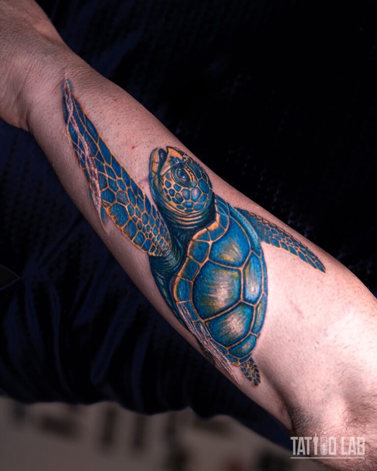 Colour sea turtle tattoo seen from above, blue shell plates outlined in gold, flippers spread along the forearm