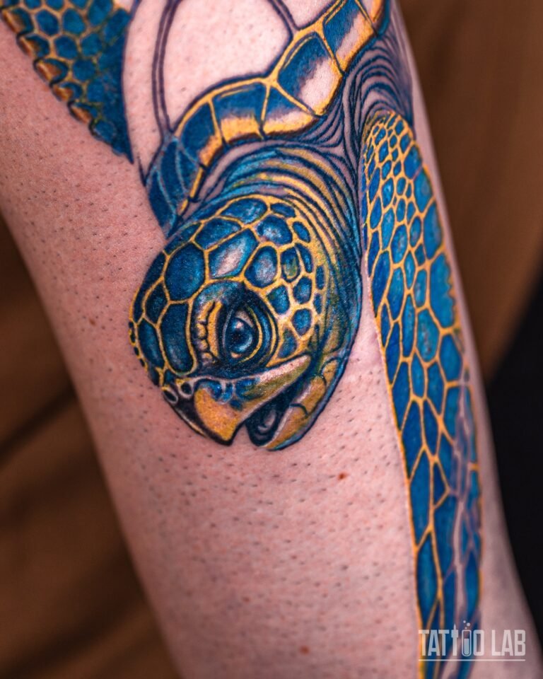 Close-up of a colour sea turtle tattoo head with a glossy dark eye and blue scales outlined in gold