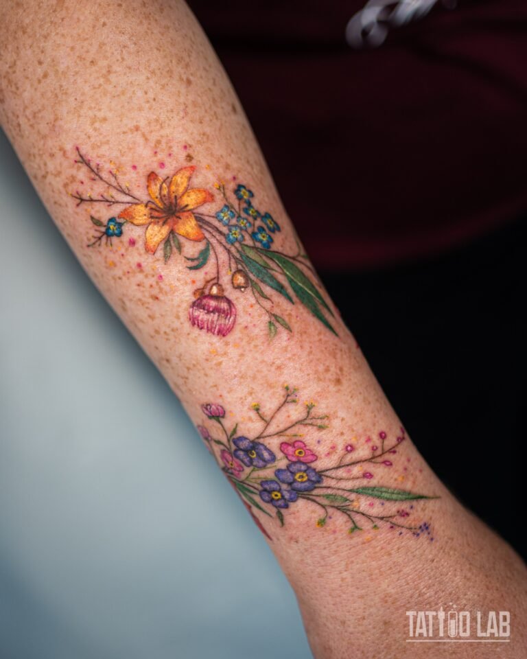 Colour wildflower tattoo on the forearm with an orange lily, blue forget-me-nots, pink blossoms and purple flowers