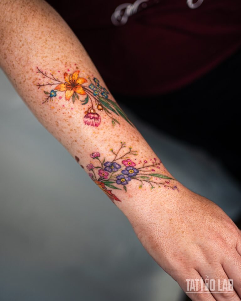 Colour wildflower tattoo wrapping around the forearm and wrist, purple and pink flowers meeting a red maple leaf