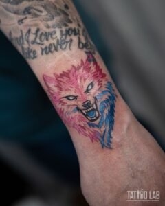 Snarling wolf head tattoo in illustrative colour with pink and blue fur on the lower forearm near the wrist