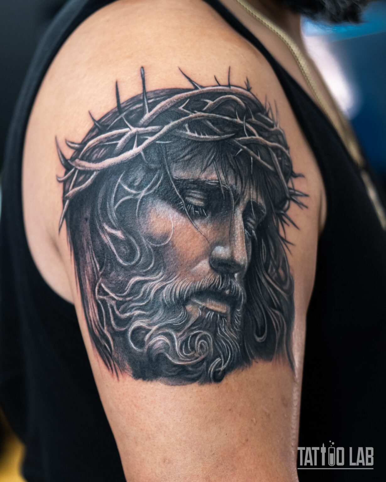 Black and grey realism cover-up tattoo of Jesus wearing the crown of thorns, on the upper arm, Tattoo Lab, Halifax