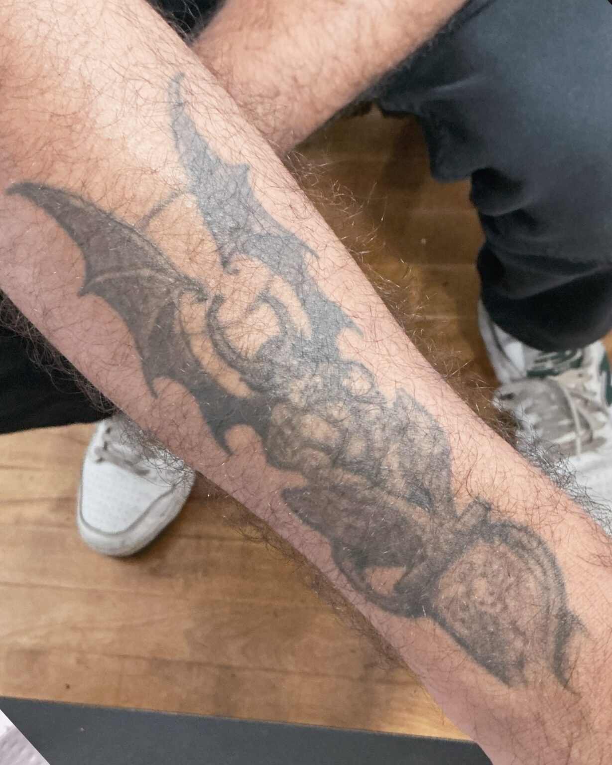 Faded grey tattoo of a winged creature along the forearm, before its cover-up at Tattoo Lab, Halifax