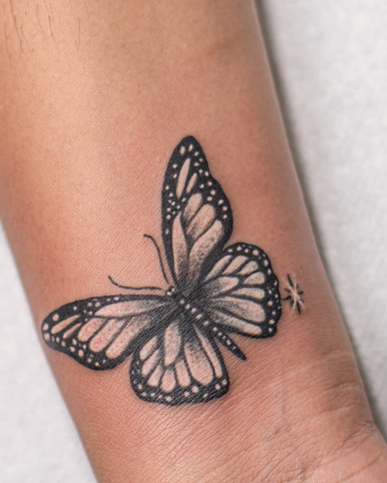 Black and grey cover-up tattoo of a butterfly with dotwork wings and a small sparkle, on the inner wrist, Tattoo Lab, Halifax