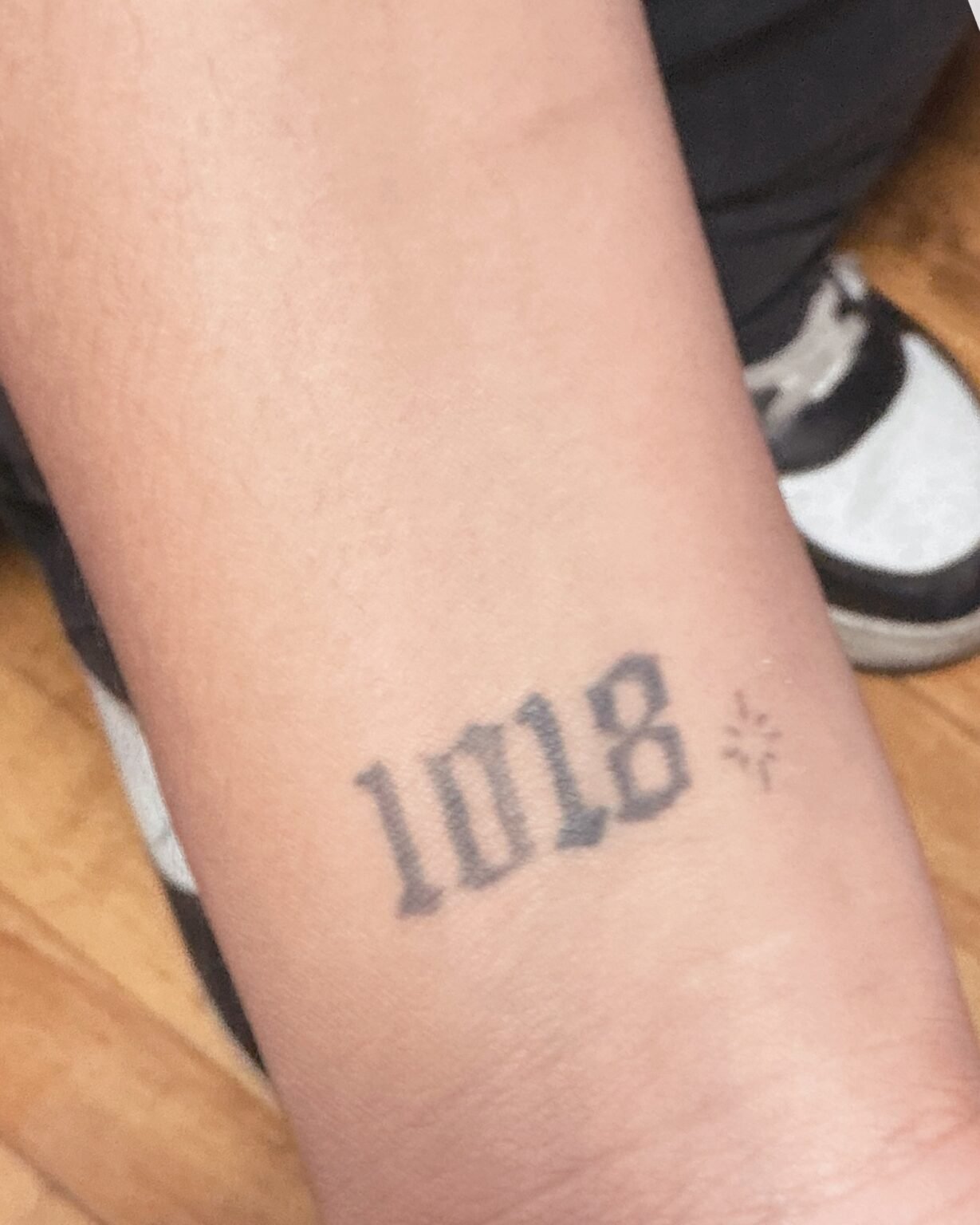 Small faded number tattoo in black script on the inner wrist, before its cover-up at Tattoo Lab, Halifax