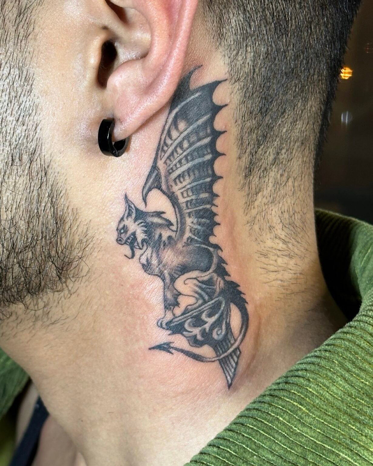 Black and grey cover-up tattoo of a winged gargoyle with a curled tail on the side of the neck, Tattoo Lab, Halifax
