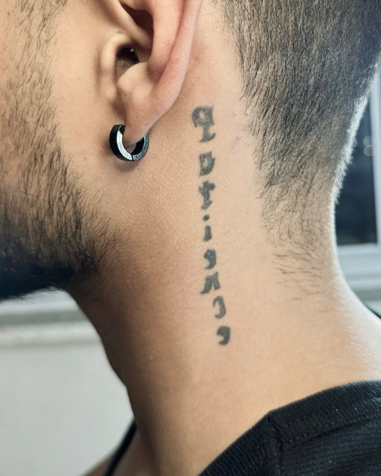 Faded vertical lettering tattoo on the side of the neck below the ear, before its cover-up at Tattoo Lab, Halifax