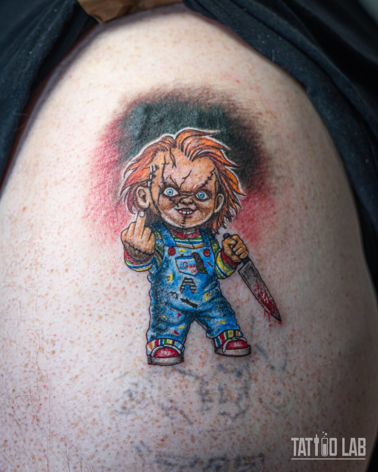 Colour cover-up tattoo of the Chucky doll holding a knife against red and black smoke, on the shoulder, Tattoo Lab, Halifax