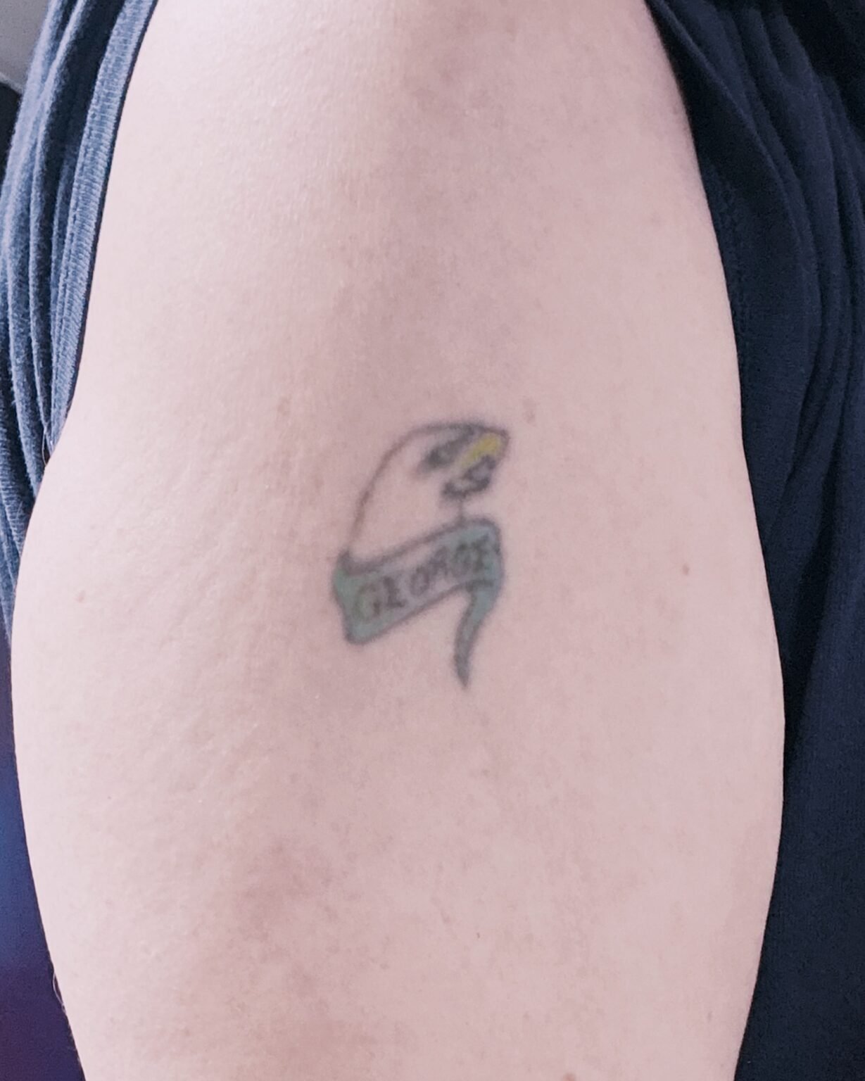 Small faded name banner tattoo on the upper arm, before its cover-up at Tattoo Lab, Halifax