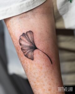 Fine line ginkgo leaf tattoo with delicate veins and soft grey shading on the upper arm