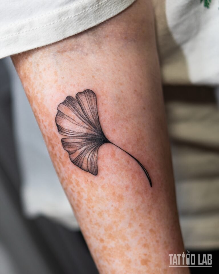 Fine line ginkgo leaf tattoo with delicate veins and soft grey shading on the upper arm