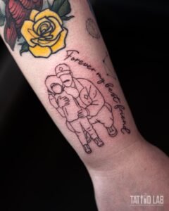 Fine line outline tattoo of an adult hugging a child with "Forever my best friend" script on the inner forearm