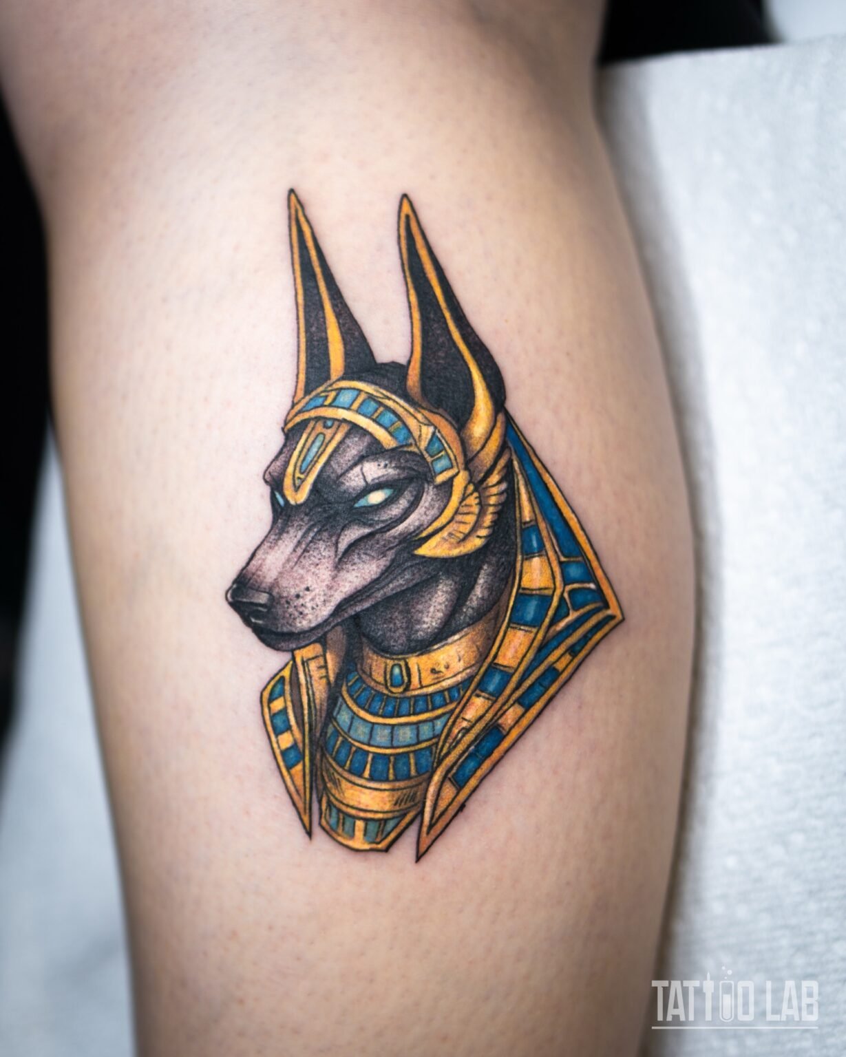 Neo-traditional Anubis head tattoo with a gold and turquoise headdress and collar, the full piece on the leg, Tattoo Lab, Halifax