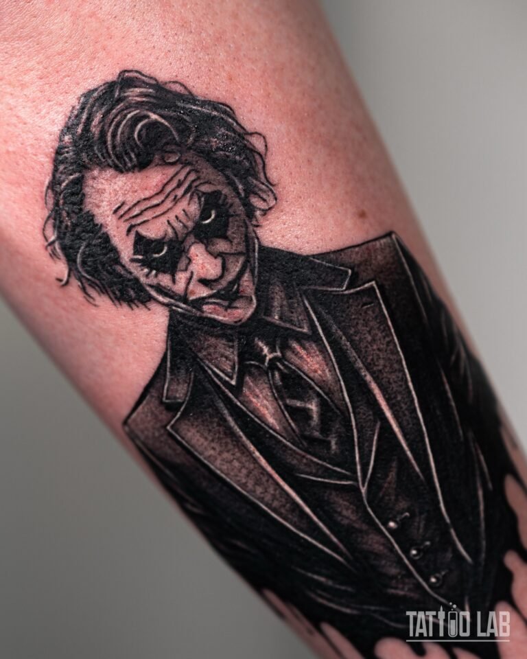 Close-up of a Joker-inspired portrait tattoo showing the shaded face, hair and dark suit on the forearm
