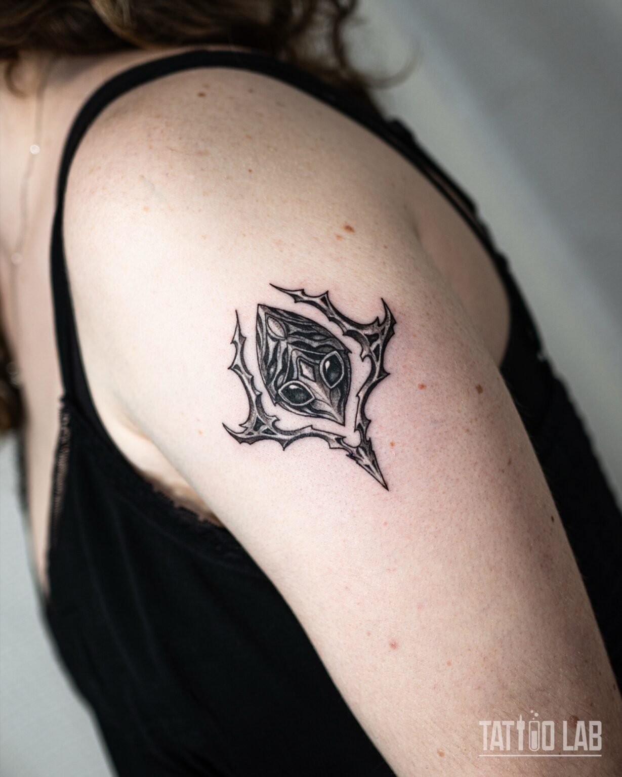 Black and grey ornamental gem tattoo framed by sharp thorn-like gothic flourishes on the upper arm, Tattoo Lab, Halifax