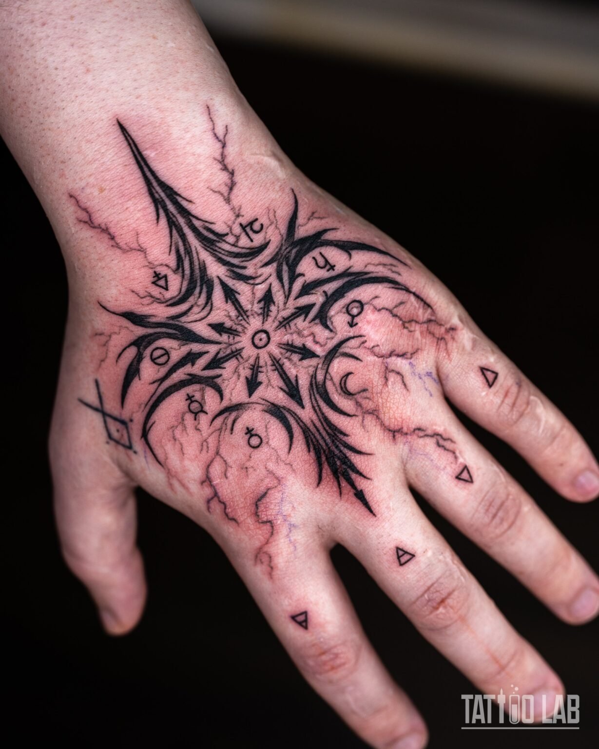 Neo-tribal chaos star tattoo with spiky black shapes, planetary symbols and lightning cracks on the back of the hand, Tattoo Lab, Halifax